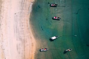 Aerial shot of anchored boats along a clear tropical beach, showcasing crystal waters.