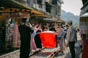Group of tourists releasing red lanterns at Jiufen Street market under a sunny sky.